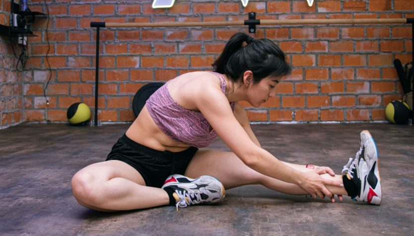 Woman performing stretches on gym floor, promoting exercise flexibility.